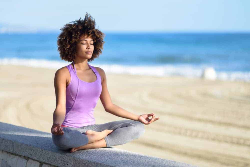A woman meditating on the beach to reduce eczema flare-ups by managing stress.