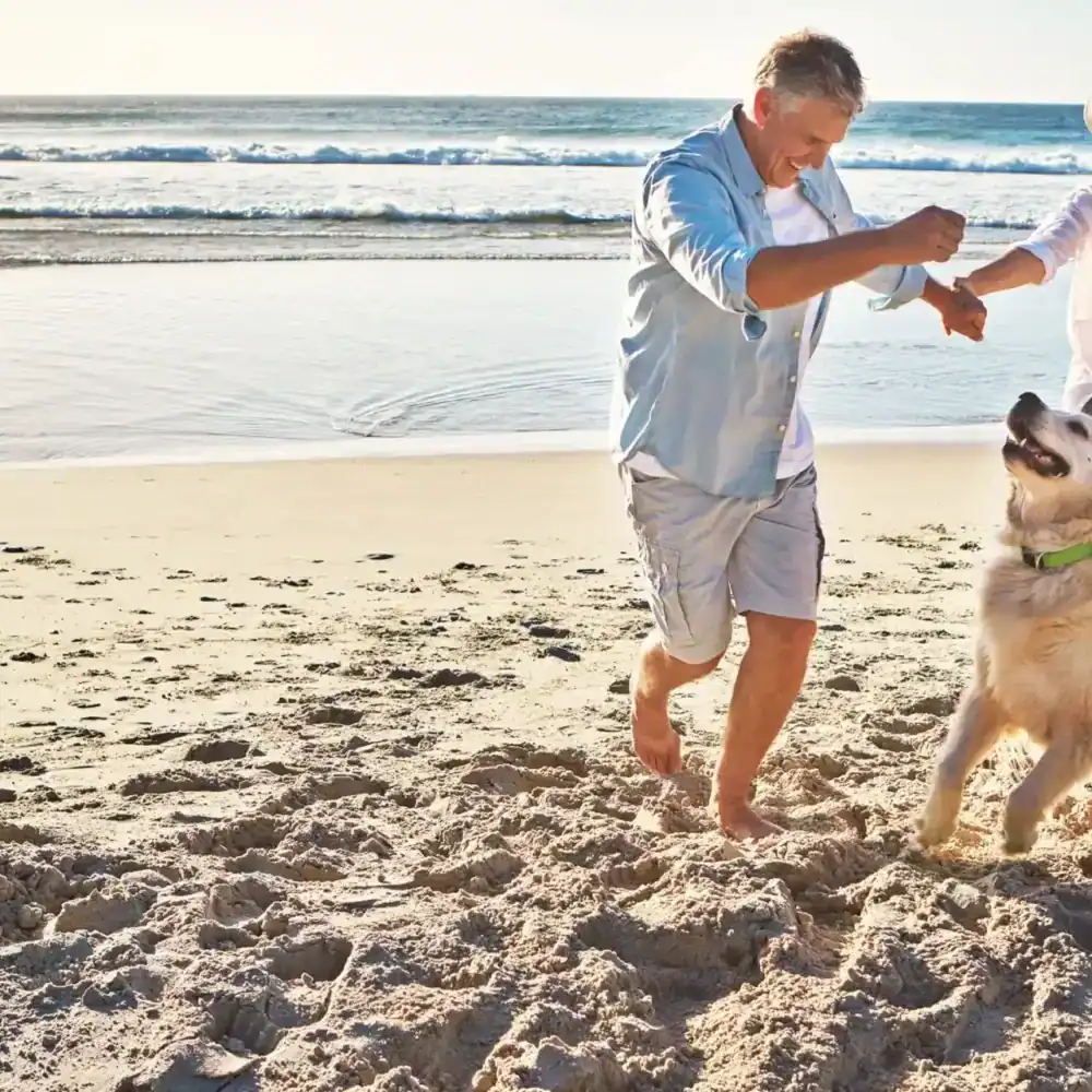 middle-aged couple playing on the beach with their dog