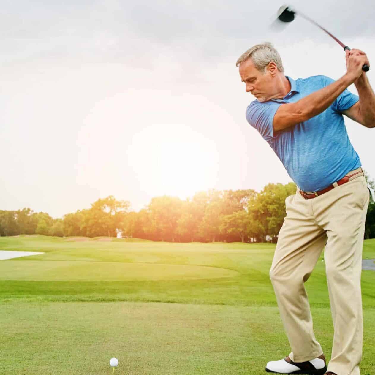 Older man takes a golf swing on a beautiful day on the course