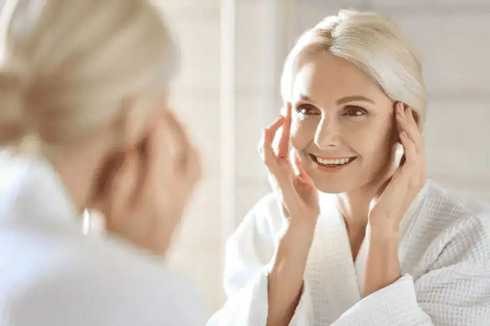 Older woman with beautiful skin smiles at reflection in the mirror