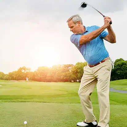 Older man takes a golf swing on a beautiful day on the course